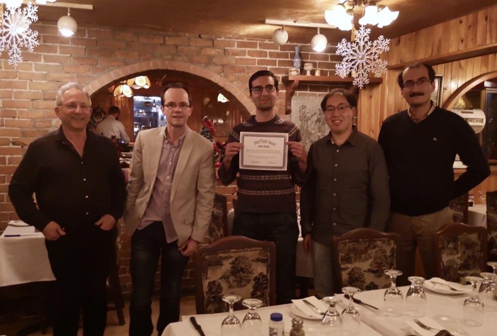 A group of men is posed standing in a restaurant. One of them is holding up an award certificate.